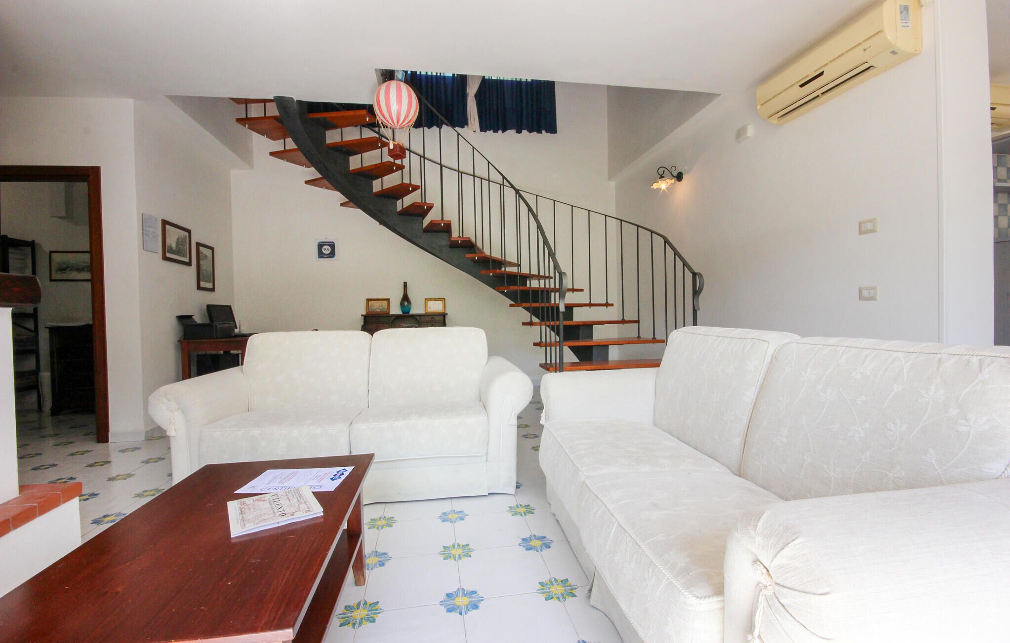 A living room with a staircase, white sofas, a wooden coffee table, and a patterned floor.