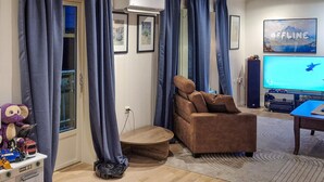 Een woonkamer met een bruine fauteuil, een grote flatscreen-tv en een robotstofzuiger.