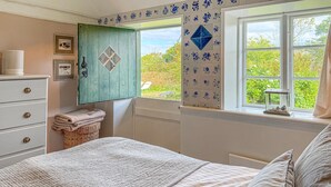 A bedroom with a bed, a dresser, a window with a view of greenery, and a decorative wall panel.