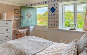 A bedroom with a bed, a dresser, a window with a view of greenery, and a decorative wall panel. - 2 bedroom beautiful home in Fanø (Fanø)