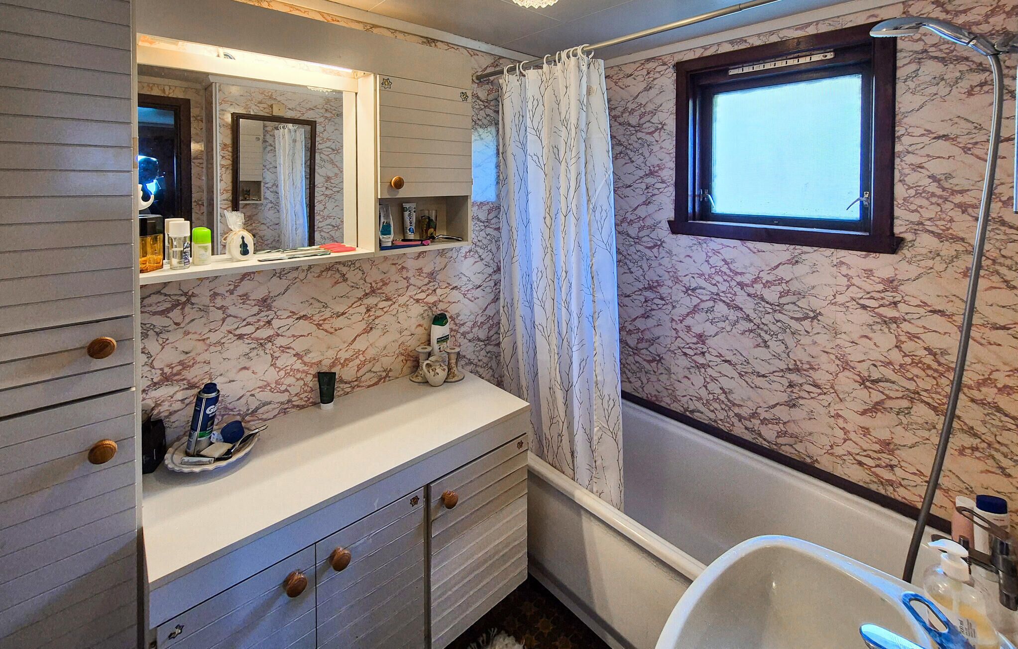 Un bagno con una parete in marmo, un lavandino, uno specchio, una doccia e una finestra.