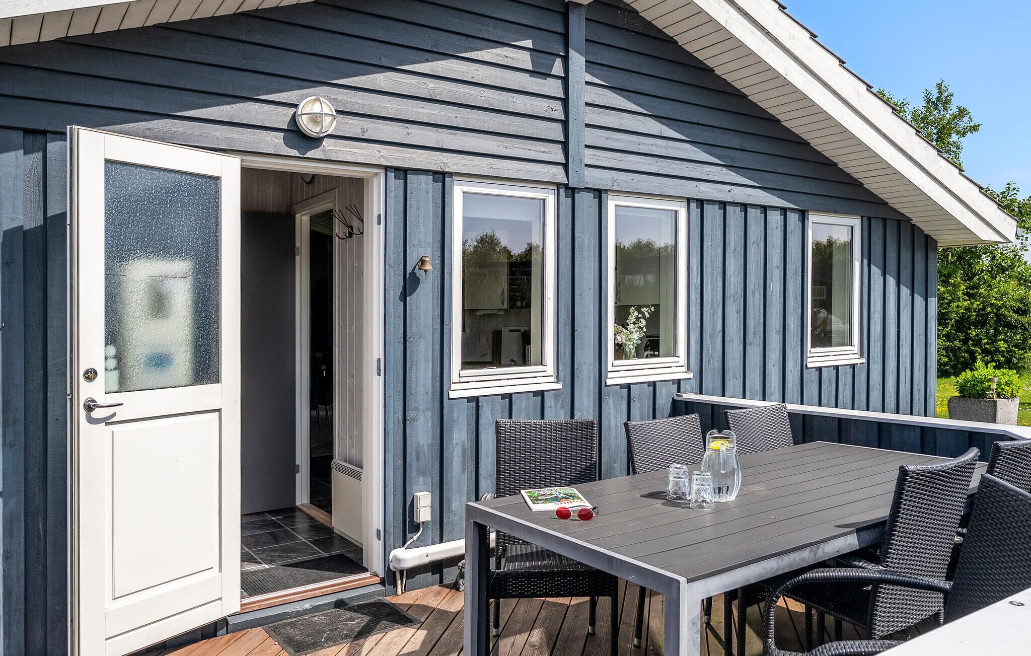 A wooden house with a sliding door, a dining table with chairs, and a small garden area.