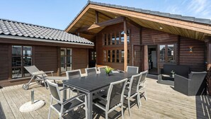A wooden cabin with a deck, outdoor seating, and a large table.