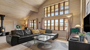 A cozy living room with a fireplace, leather sofa, and large windows offering a view of the outdoors.