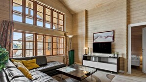 A spacious living room with a leather sofa, a glass coffee table, and a large window with curtains.