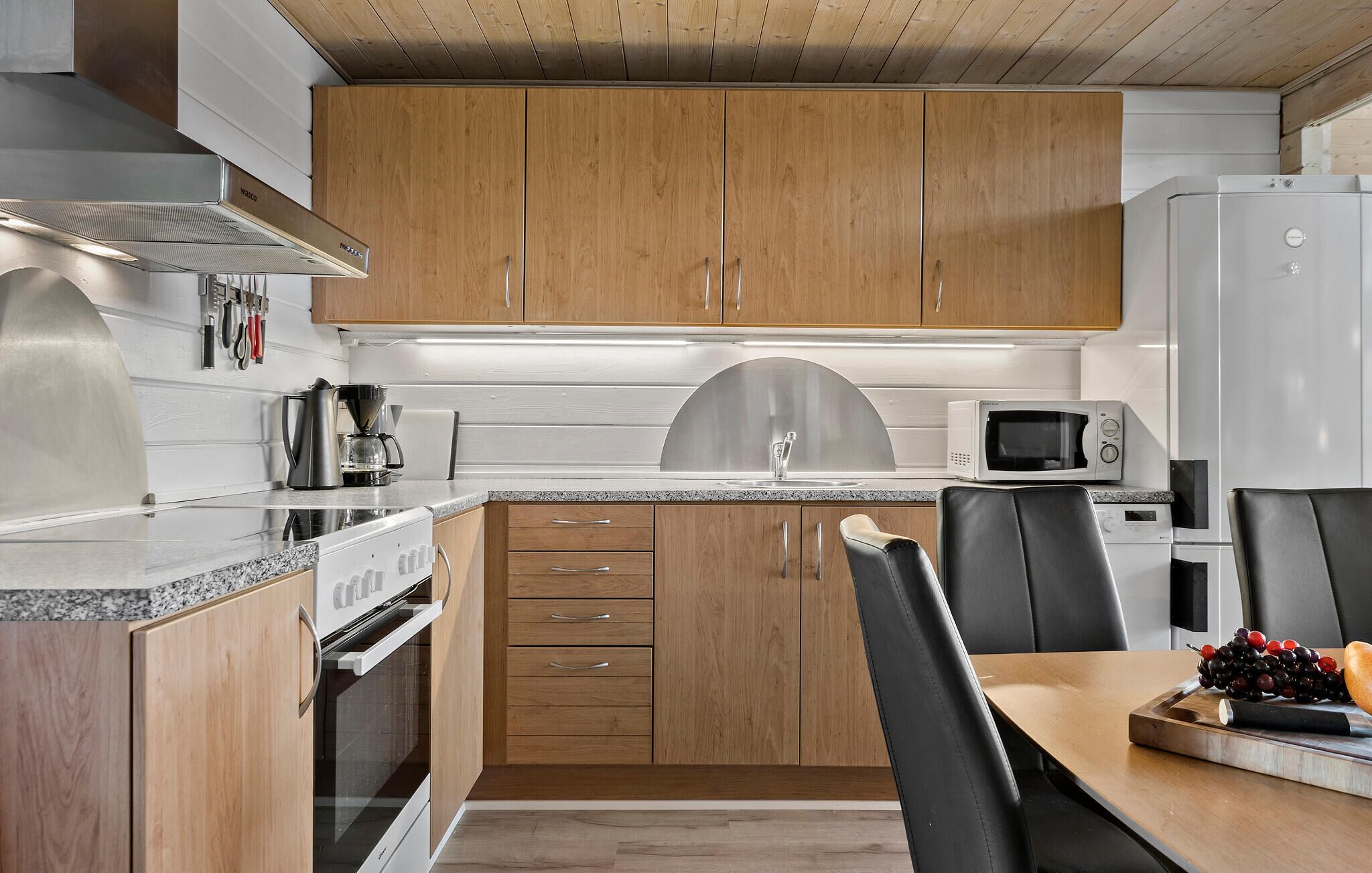 A modern kitchen with wooden cabinets, stainless steel appliances, and a dining area with a table and chairs.