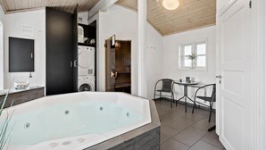 A bathroom with a large bathtub, a washing machine, and a small table with chairs.
