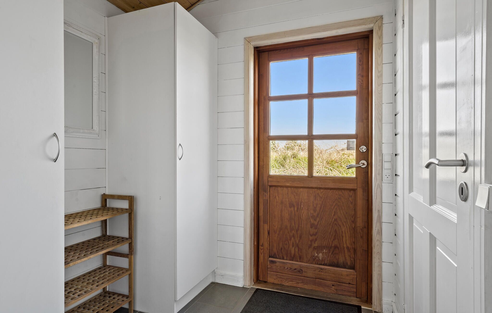 A wooden door with a window, a white door with a handle, and a wooden shelf unit.