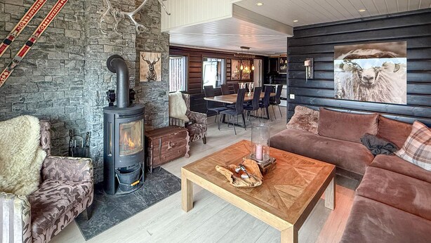 Una sala de estar acogedora con pared de piedra, chimenea, sofá y comedor con mesa de madera.