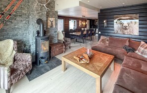 A cozy living room with a stone wall, a fireplace, a sofa, and a dining area with a wooden table. - Gorgeous home in Hovden i Setesdal with sauna (Hovden i Setesdal)