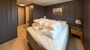 Un dormitorio con una cama grande, una mesita de noche de madera, una lámpara y una puerta que da a otra habitación.