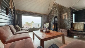 Un salón acogedor con chimenea de piedra, sofá de cuero y un gran ventanal con vistas al exterior.