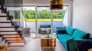 A modern living room with a green sofa, wooden coffee table, and a view of a green landscape through large glass doors. - Awesome apartment in Nowecin with sauna (Nowecin)