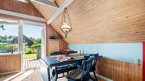 A dining area with a wooden table and chairs, a hanging light fixture, and a view of the outdoors.
