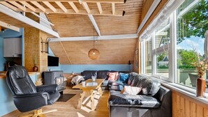 A cozy living room with a fireplace, leather furniture, and large windows offering a view of the outdoors.