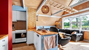 A modern kitchen with a wooden ceiling, a brick accent wall, and a dining area with a black leather sofa and wooden table.