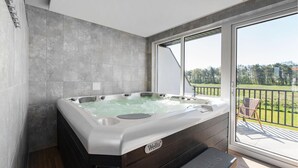 A modern bathroom with a large hot tub, a bench, and a view of a green landscape through large sliding doors. - Cozy apartment in Nowecin with sauna (Nowecin)