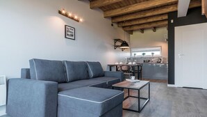 A modern living room with a grey sectional sofa, a small wooden coffee table, and a kitchen in the background. - Cozy apartment in Nowecin with sauna (Nowecin)