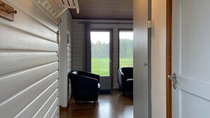 Ein Korridor mit weißem Wandpaneel, zwei schwarzen Stühlen und einer Tür, die auf einen Balkon mit Blick auf ein Wiesenfeld führt.