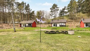 Ländliche Szenerie mit drei Blockhütten, einem Picknicktisch und einer Fahnenstange.