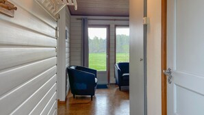 A hallway with a wooden floor, two blue chairs, and a door leading to a balcony with a view of a grassy area. - Amazing home in Degeberga (Degeberga)