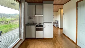 A compact kitchen with a sink, stove, and refrigerator, a small dining area with a bench, and a view of a green landscape through a window. - Amazing home in Degeberga (Degeberga)