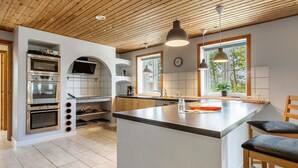 Una cocina moderna con hornos empotrados, una isla grande, iluminación colgante y vistas al exterior a través de amplios ventanales.