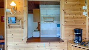 Un interior de madera con área de cocina, que incluye una cafetera y una estantería con objetos decorativos.