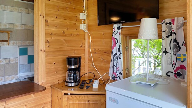 Interior de una cabaña de madera con cafetera, televisor y ventana con cortinas.