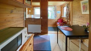 Interior de una cabaña de madera con kitchenette, una mesa de comedor y una silla roja.