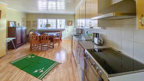 Una cocina con armarios de madera, una mesa de comedor con sillas, una alfombra verde y una ventana con vistas a árboles.