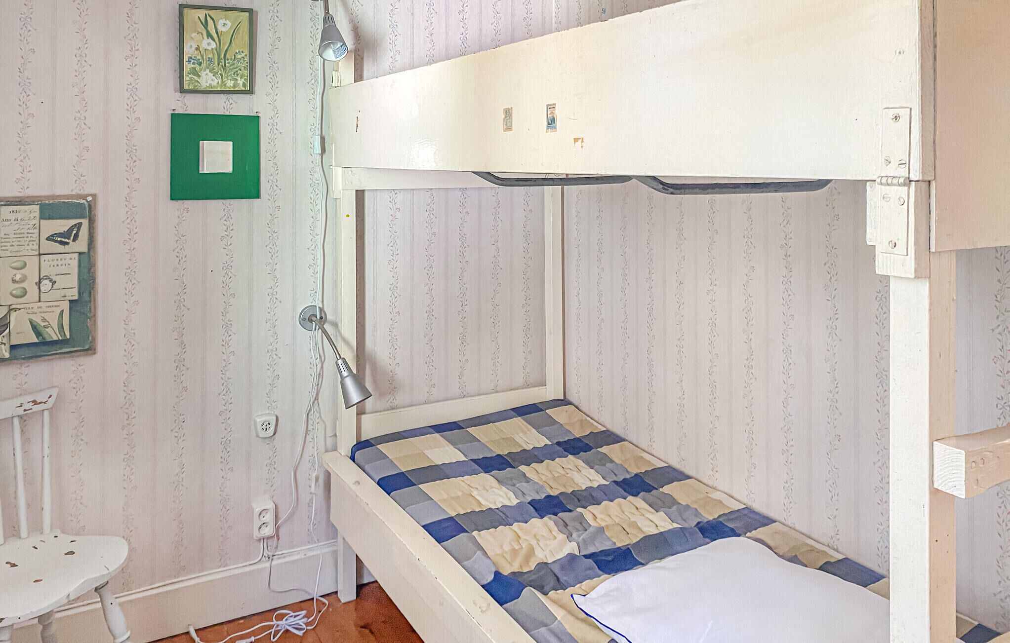 Een stapelbed met een geruit matras, een klein bureau en een wandlamp.