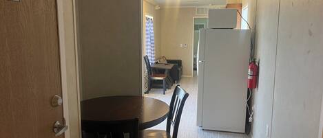 A compact kitchen with a refrigerator, a dining table with chairs, and a water heater access sign on the door.