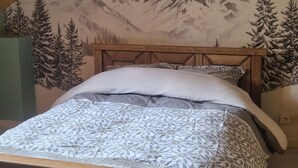 Een slaapkamer met een houten bed en een muurschildering van een berg, en een schuine plafond.