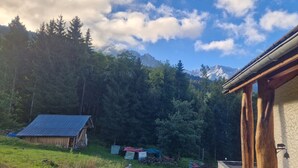Een rustieke hut met een schuin dak, omgeven door dicht bos en bergen op de achtergrond.