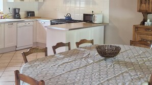 Een keuken met houten balken, witte kasten, een fornuis en een eettafel met stoelen.