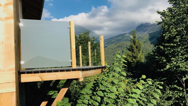 Una terraza de madera con un panel de vidrio que da a un paisaje montañoso.