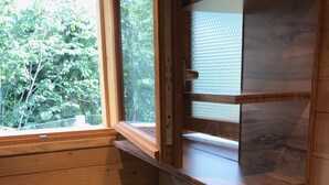 Un baño de cabaña de madera con ventana, un lavamanos y un estante de madera.