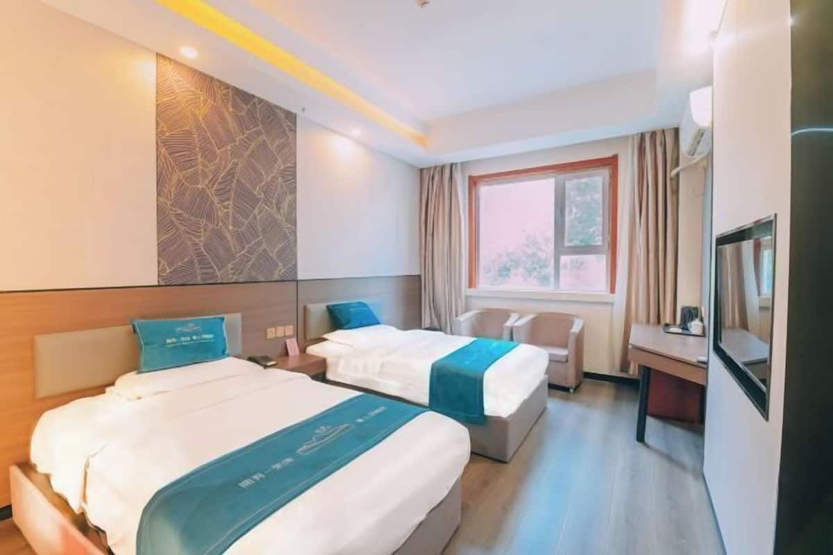 Habitación de hotel con dos camas, un escritorio, un televisor y una ventana con cortinas.