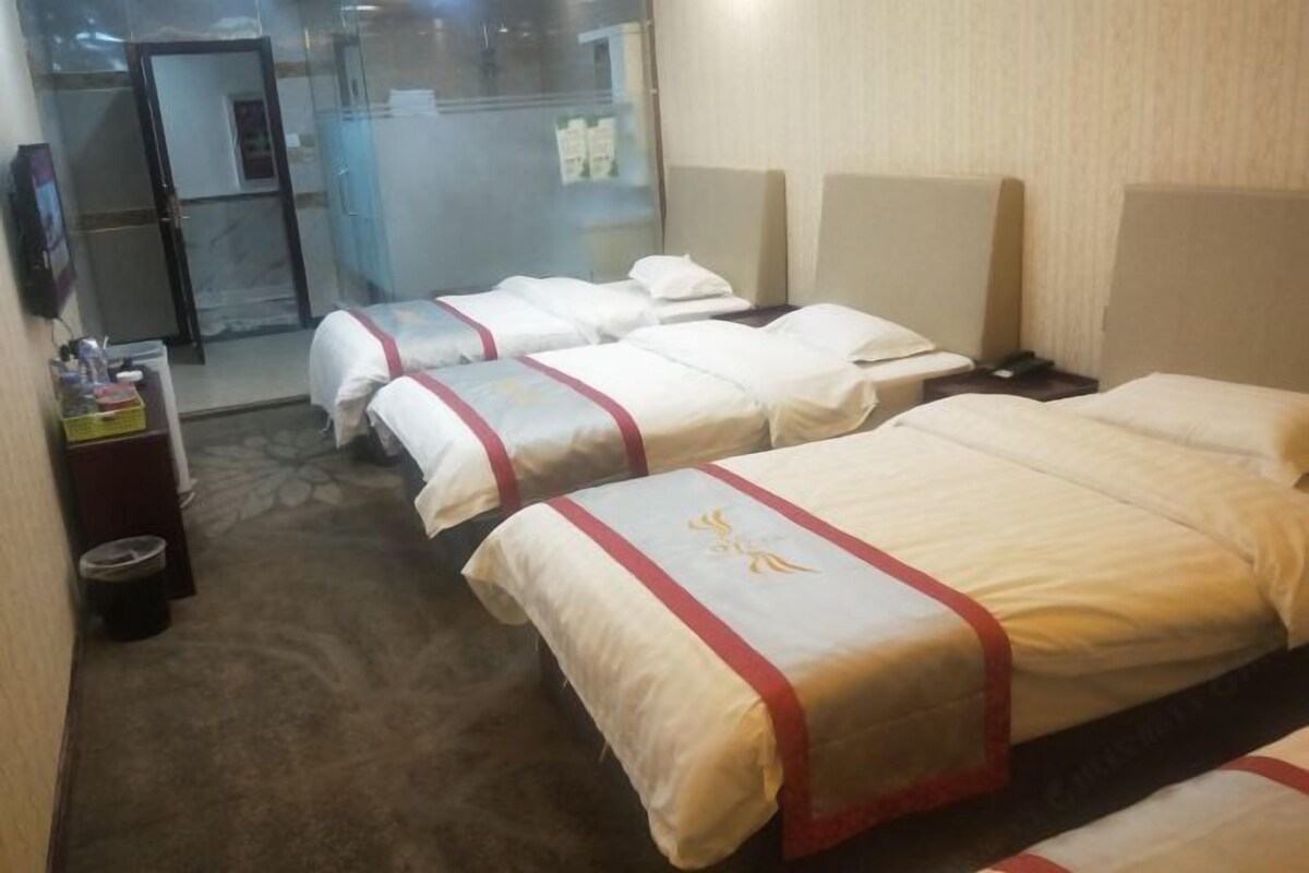 Une chambre d’hôtel avec trois lits, un petit bureau avec une poubelle et une porte en verre donnant sur la salle de bain.