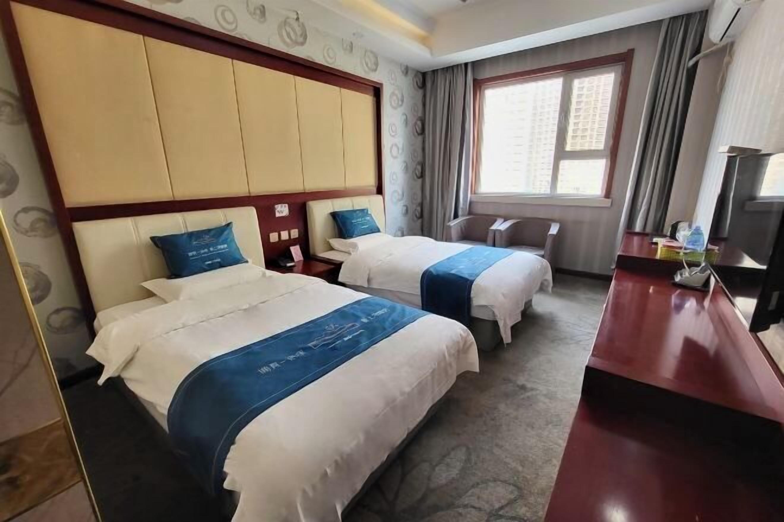 A hotel room with two beds, a desk, a TV, and a window with curtains.