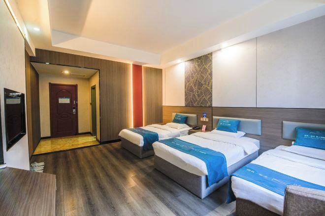 A hotel room with two beds, a wooden floor, a TV, and a door leading to another room.