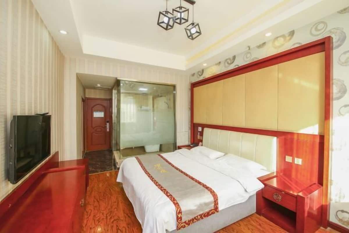 Habitación de hotel con una cama grande, televisión, suelo de madera y una puerta de vidrio que da a un baño.