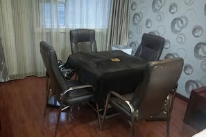 Een vergaderruimte met een zwarte tafel en lederen stoelen, een whiteboard en een raam met gordijnen.