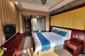 Ein Hotelzimmer mit Bett, Fernseher, Holzschrank und einem durch eine Glastür einsehbaren Badezimmer.