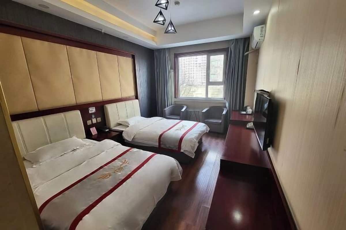 Habitación de hotel con dos camas, un escritorio, una silla, un televisor y una ventana con cortinas.