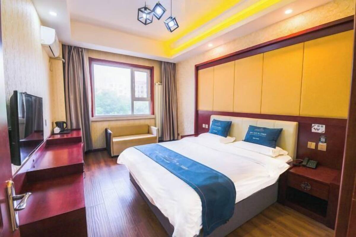 Una habitación de hotel con cama, mesita de noche, lámpara, ventana y vistas al exterior.