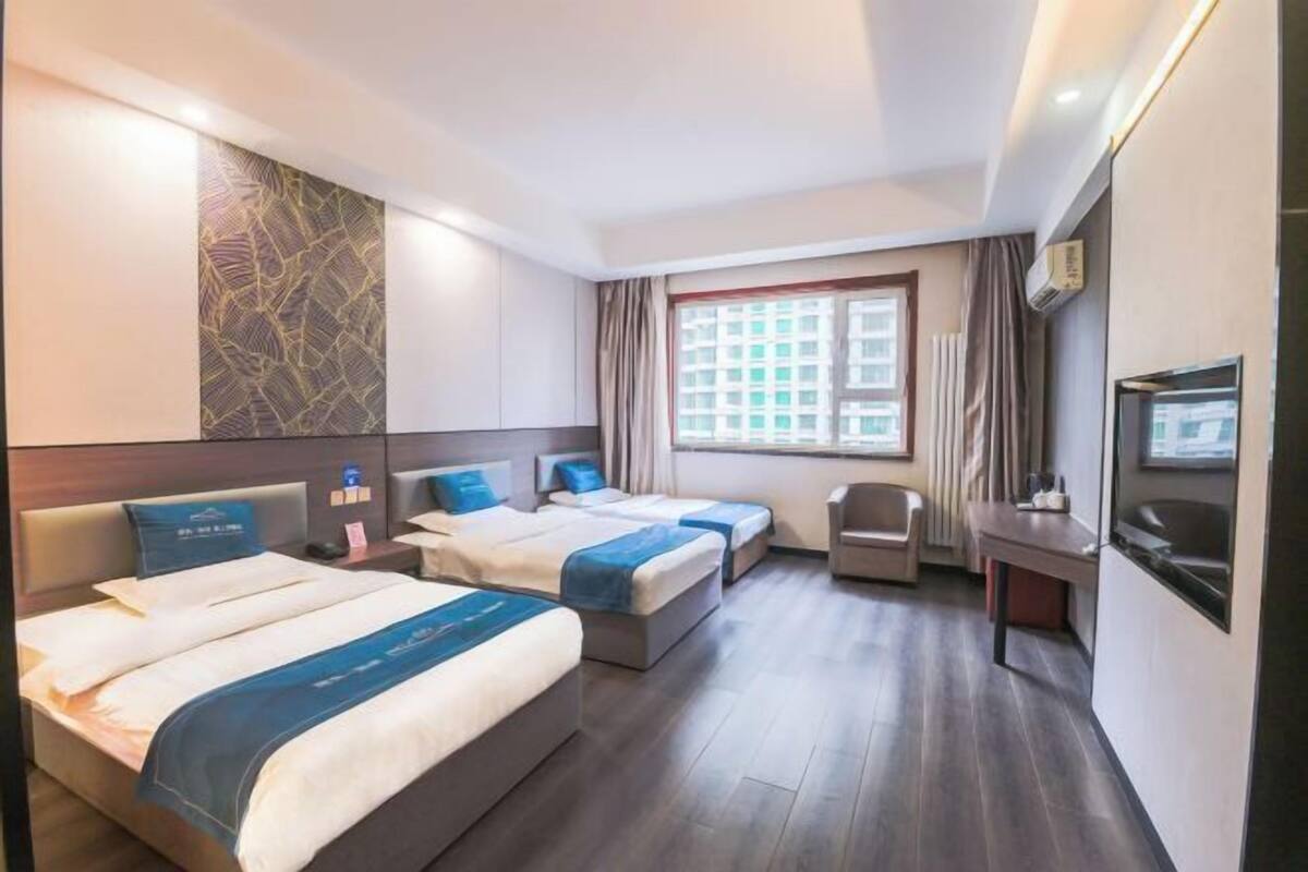 Habitación de hotel con dos camas, un escritorio, una silla, un televisor y una ventana con cortinas.