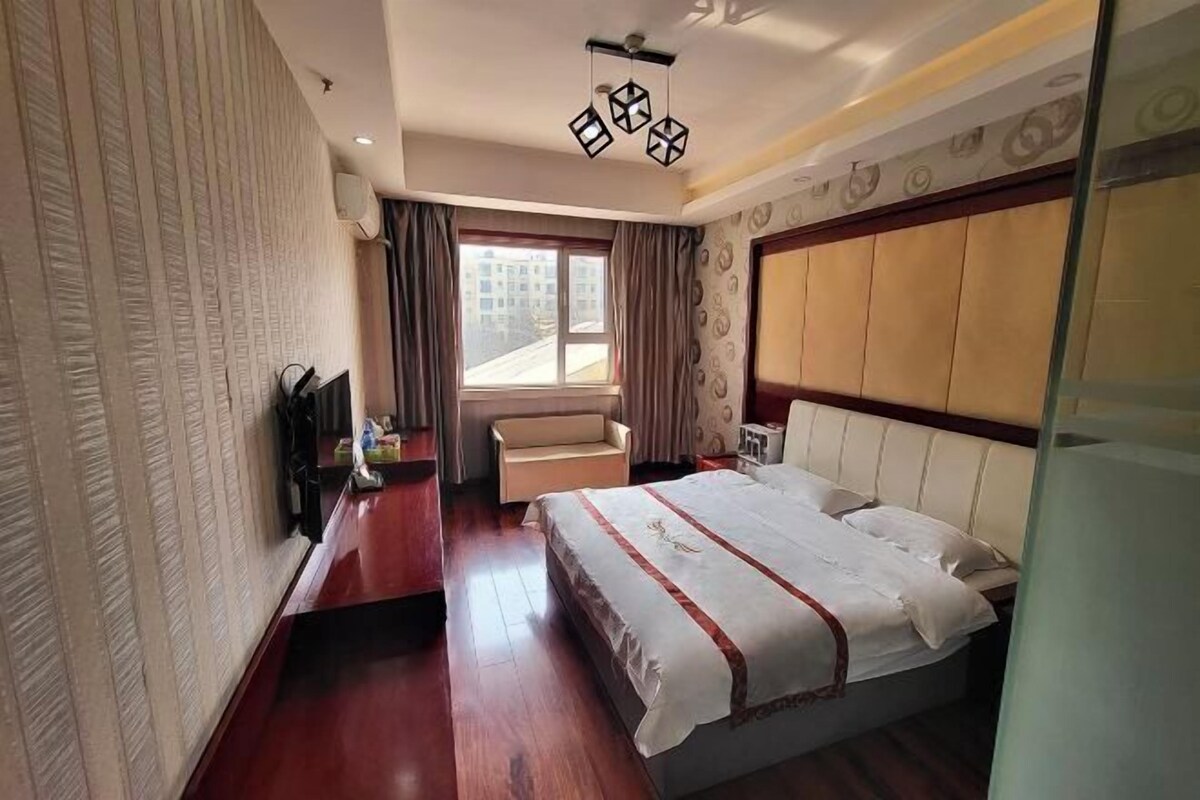 Ein Hotelzimmer mit einem großen Bett, einer Couch, einem Fernseher und einem Fenster mit Vorhängen.