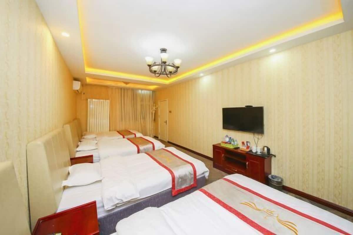 Habitación de hotel con cuatro camas, televisión, candelabro y minibar.